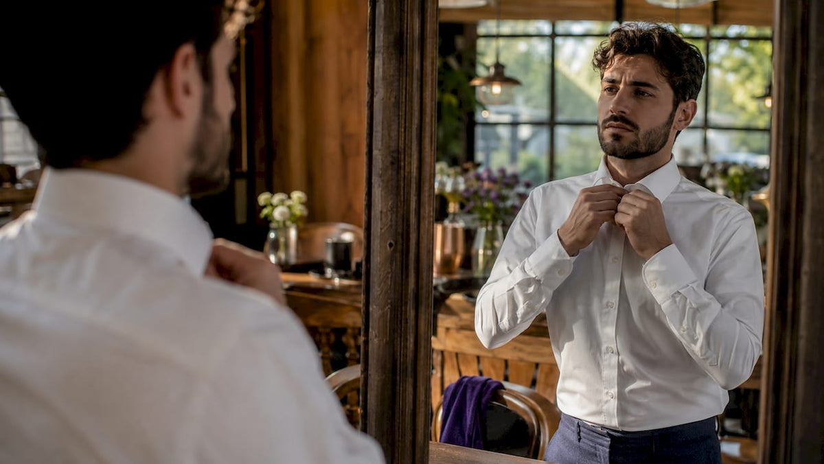 Man adjusting white spread collar shirt in mirror